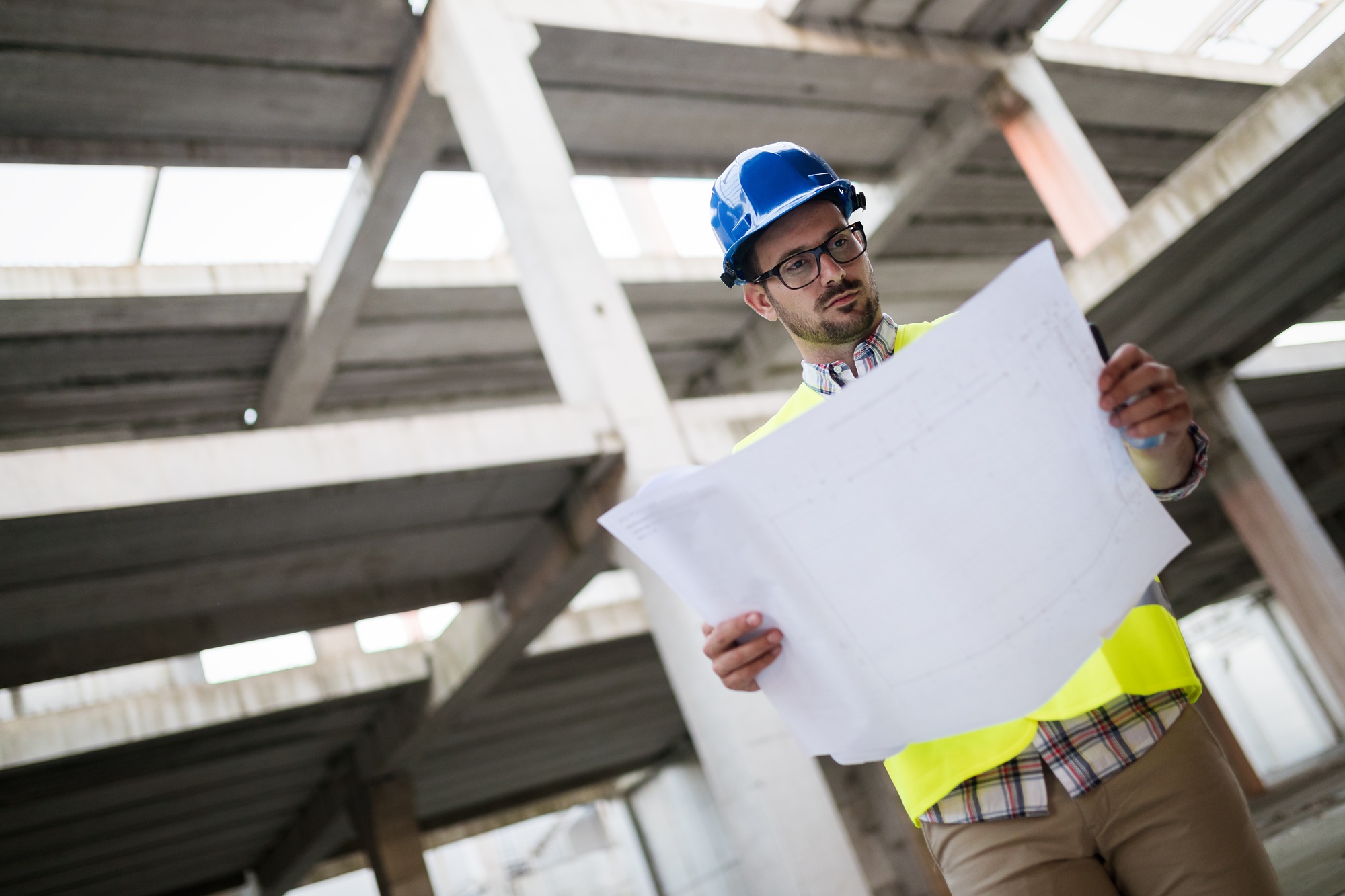 Portrait of male site contractor engineer with hard hat holding blue print paper